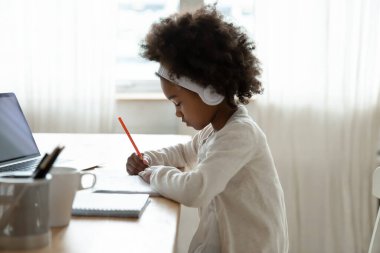 African girl wears headphones doing homework seated at desk