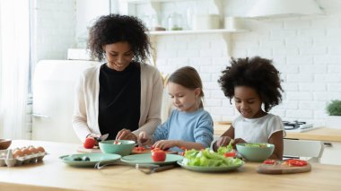 African mum two daughters cutting fresh vegetables preparing salad