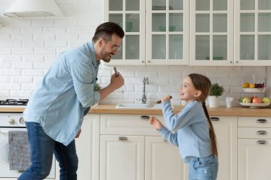 Dad and little daughter singing in kitchen enjoy weekend fun