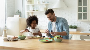 Stepfather teaches african daughter cut diverse vegetables for vegetarian salad