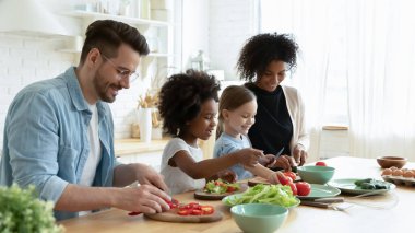 Full multinational family preparing dietary vegetable salad in kitchen