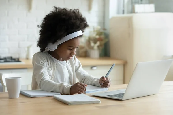 African schoolgirl in headphones using laptop do homework at home — Stock Photo, Image