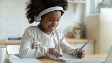African schoolgirl sit at table writing in workbook studying distantly