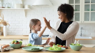 Caucasian daughter preparing salad with African mother in kitchen