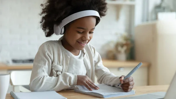 African schoolgirl sit at table writing in workbook studying distantly — Stock Photo, Image