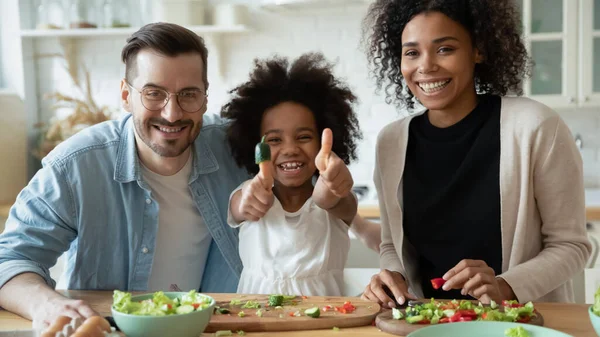 Cheerful multiethnic couple with daughter cooking together in kitchen — Stock fotografie