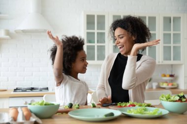 Excited African mom and little daughter cooking together in kitchen