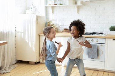 Small multi ethnic girls holding hands play in kitchen