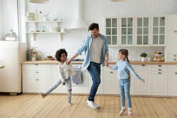 Caucasian father multiethnic daughters dancing in modern cozy kitchen — Stok fotoğraf