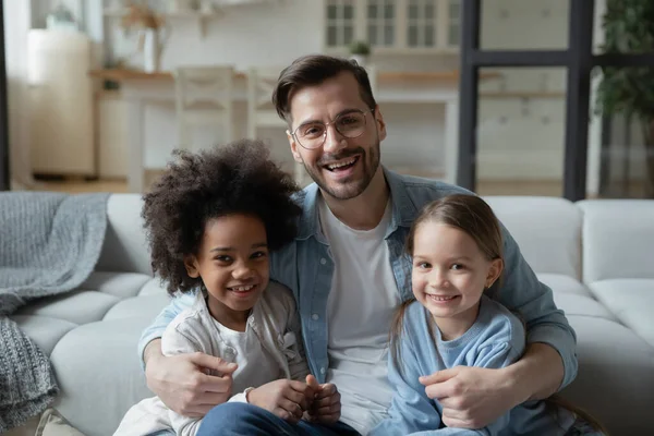 Father sit on sofa hugs caucasian and african little daughters — Stockfoto