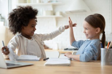 Multiethnic girls distracted from homework playing seated at table indoor