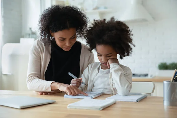 African mother helps with task to little schoolgirl daughter — Stock Photo, Image