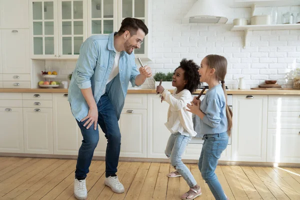 Daddy with daughters having fun dancing and singing in kitchen