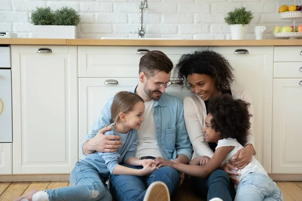 Familia de propietarios multinacionales con hijas descansando en piso de cocina moderna — Foto de Stock