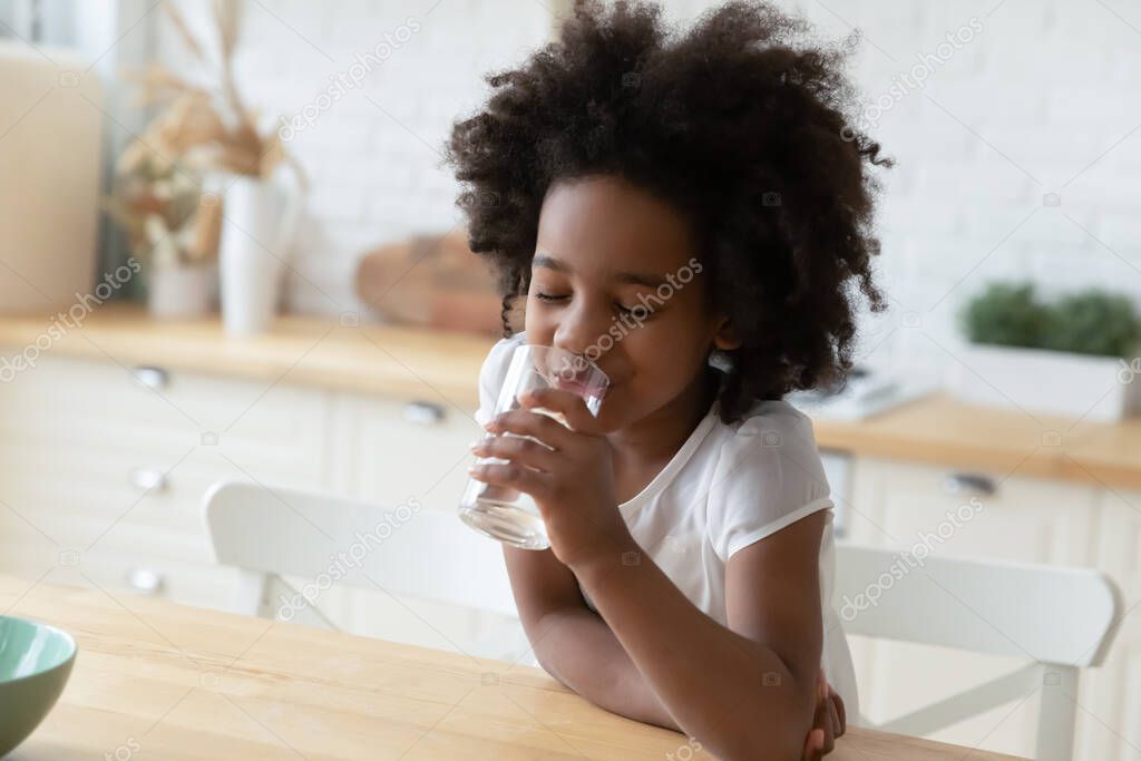 African little girl drinking natural water seated in kitchen