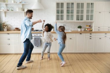 Caucasian father multiracial daughters dancing together in modern cozy kitchen