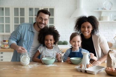 Multiethnic family with daughters engaged in cake preparation in kitchen