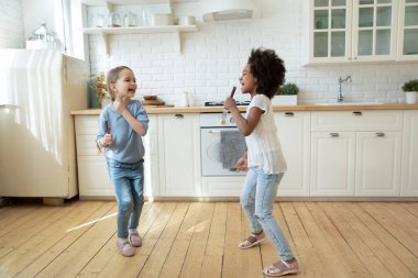 Little multiethnic girls play in kitchen singing songs and dancing
