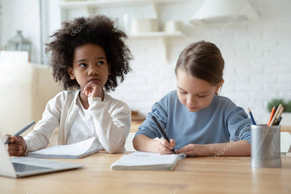 Multiethnic sisters do homework seated at table in kitchen