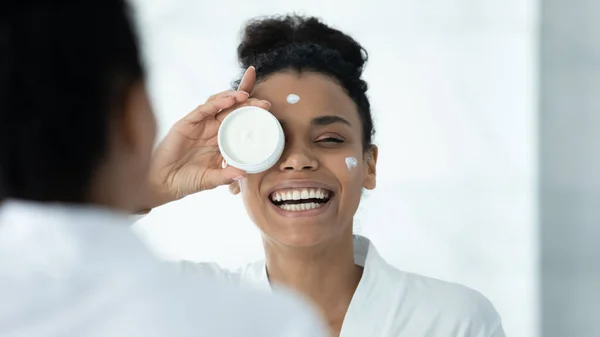 Mirror reflection funny African American woman holding face cream jar — Stockfoto