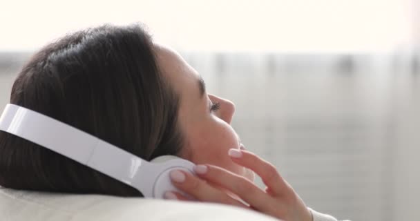 Tranquil young beautiful woman enjoying listening favorite music in earphones. — Stockvideo