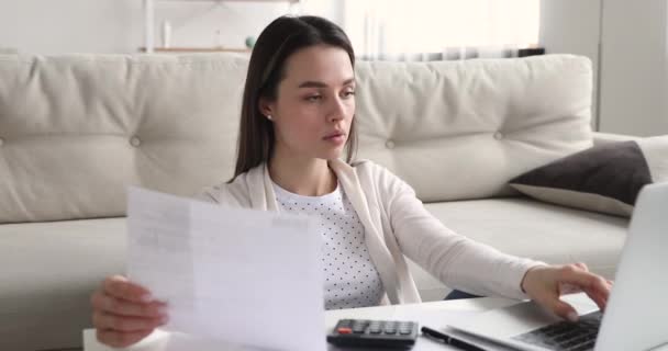 Jeune femme concentrée détenant un reçu papier, utilisant l'application e-banking. — Video