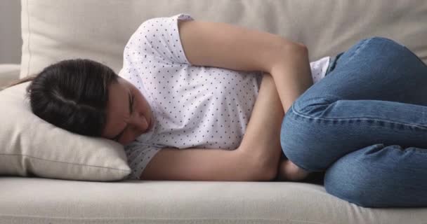 Напряженная молодая женщина лежит на диване, страдает от боли в животе . — стоковое видео