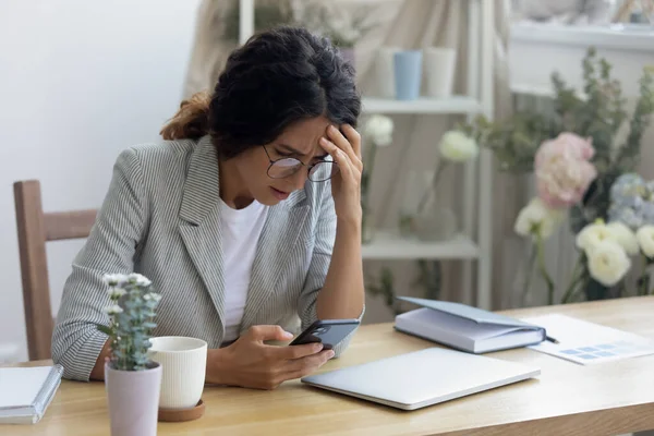 Δυστυχισμένη γυναίκα κάθεται στο γραφείο απογοητευμένη από το μήνυμα στο κινητό — Φωτογραφία Αρχείου