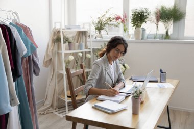 Beyaz kadın tasarımcı dizüstü bilgisayarda çalışıp notlar alıyor.