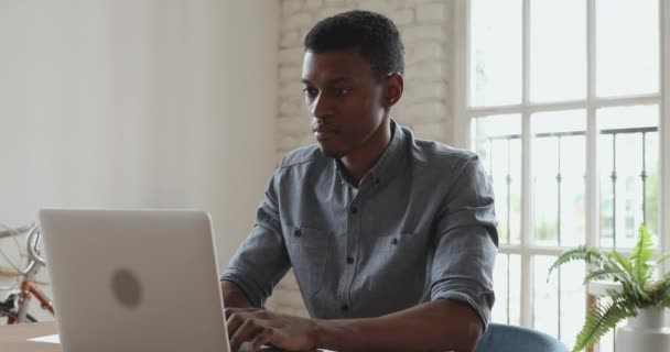 Ernstige Afrikaanse zakenman werkt aan laptop doet papierwerk in kantoor — Stockvideo