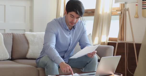 Soustředěný mladý pohledný muž dělá finanční papírování doma — Stock video
