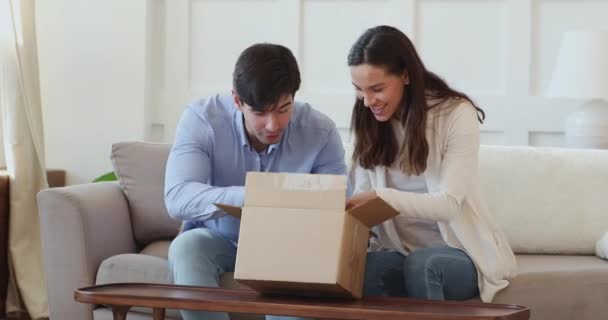 Curious happy young married couple clients unpacking cardboard box. — Stock Video