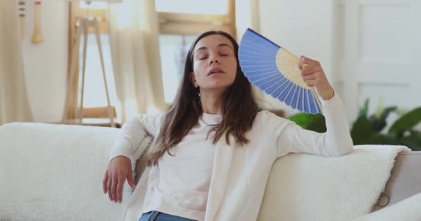 Cansada milenar senhora soprando vento com ventilador de papel em casa . — Vídeo de Stock