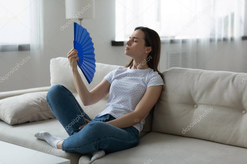 Woman suffers from unbearable hot weather waving fan cooling herself
