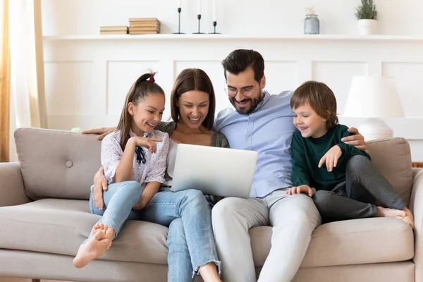 Счастливая семья с детьми отдыхает на диване с ноутбуком — стоковое фото