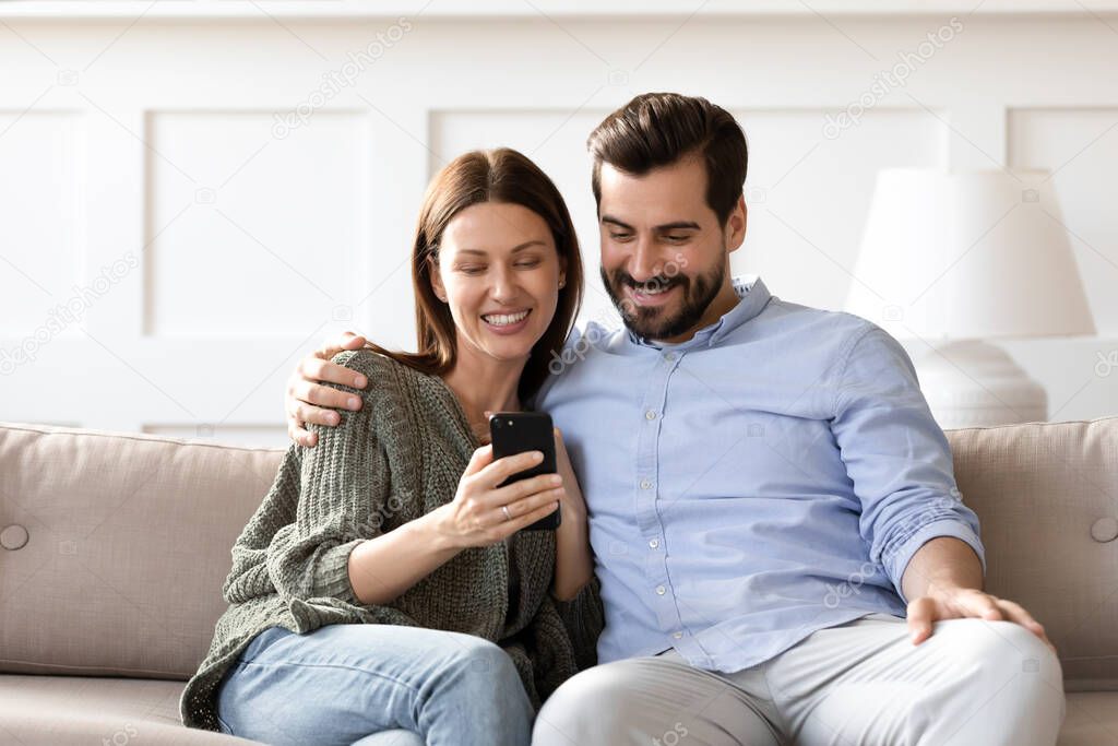 Smiling man and woman hugging, using smartphone together, having fun