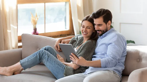 Mutlu genç çift kanepeye uzanıyor, birlikte bilgisayar tableti kullanıyorlar. — Stok fotoğraf