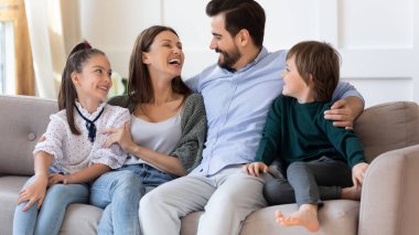 Mutlu anne ve baba çocuklarla kucaklaşıyor, kanepede oturuyor.