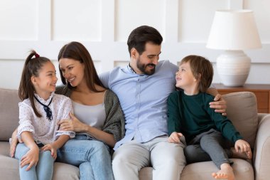 Mutlu ebeveynler çocuklarla kucaklaşır, rahat koltukta otururlar.