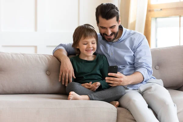 Happy father with little son using smartphone, sitting on couch
