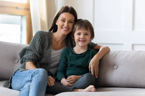 Retrato familiar madre sonriente abrazando a su hijo pequeño, sentado en el sofá —  Fotos de Stock