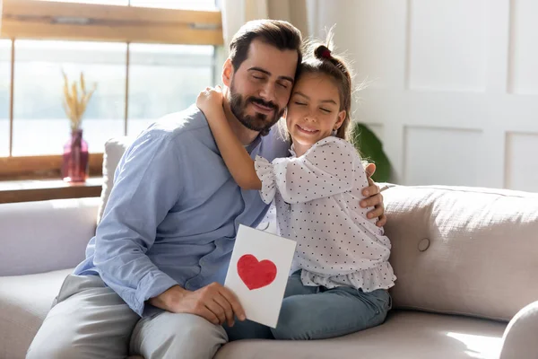 Hübsches Mädchen gratuliert Vater, umarmt ihn, präsentiert Grußkarte — Stockfoto