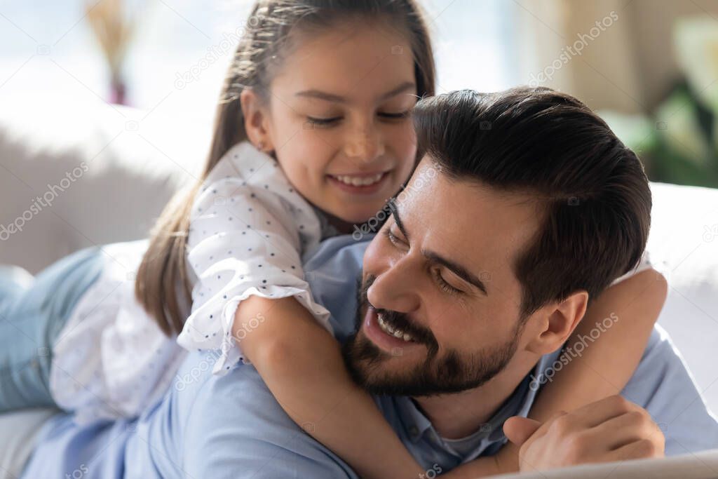 Happy father and little daughter hugging, lying on couch together