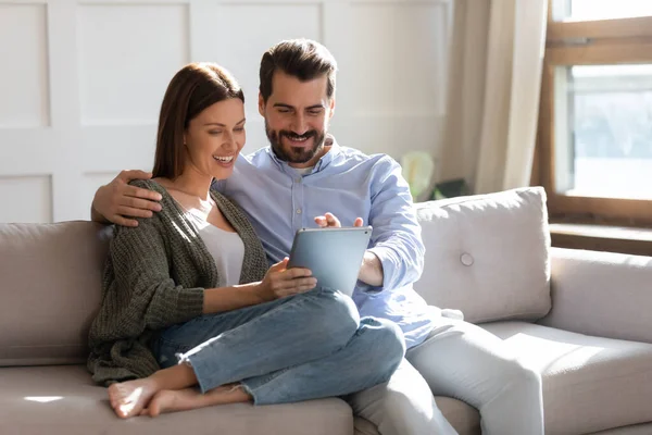 Glückliches junges Paar, das zusammen mit einem Tablet-Computer auf der Couch sitzt — Stockfoto