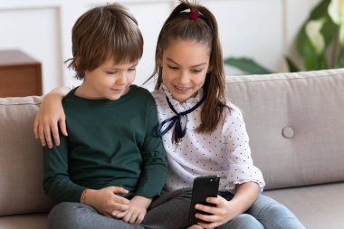 Mutlu küçük kız ve erkek kardeş evde akıllı telefon kullanıyor.
