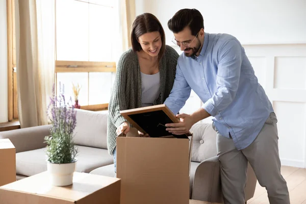 Feliz pareja joven desempacando pertenencias, sosteniendo el marco con la foto — Foto de Stock