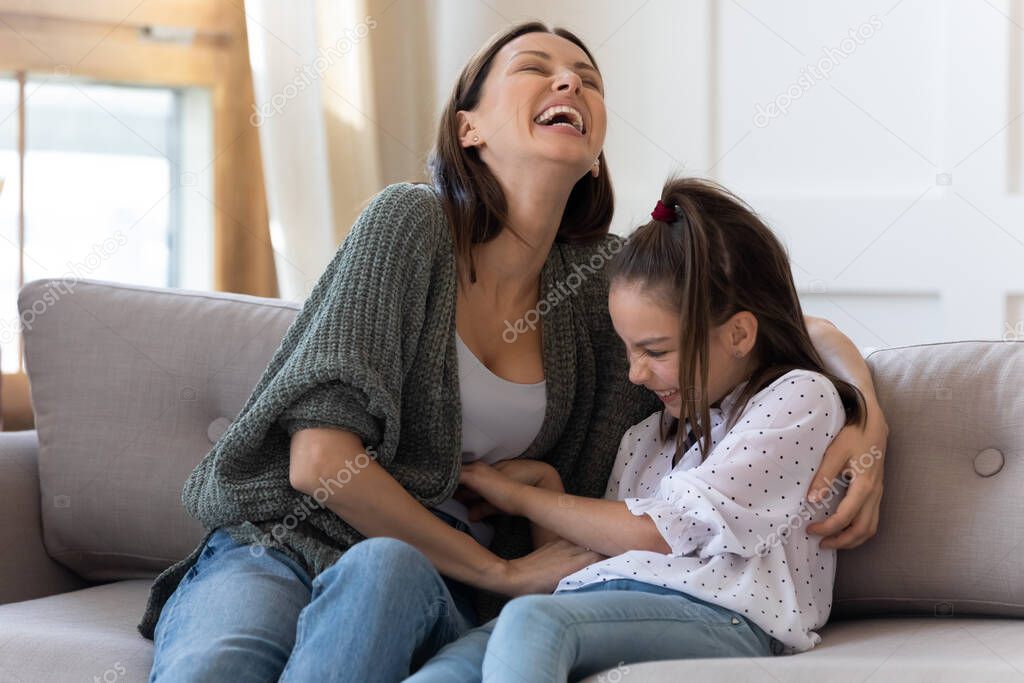 Happy mother tickling adorable daughter, playing funny game at home