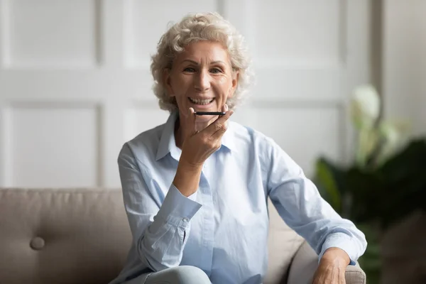 Volwassen vrouw zitten op de bank zeggen voice message met behulp van smartphone — Stockfoto