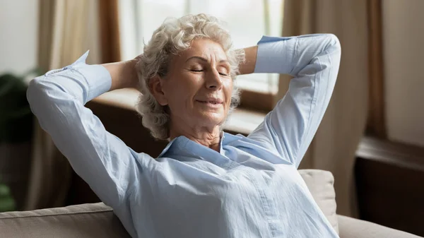 Calm mature woman puts hands behind head resting at home — Stock Photo, Image
