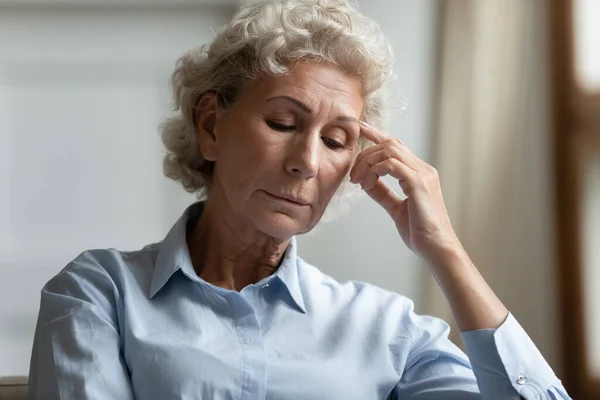 Elderly woman looks concerned sitting indoors thinking about life troubles — Stock Photo, Image